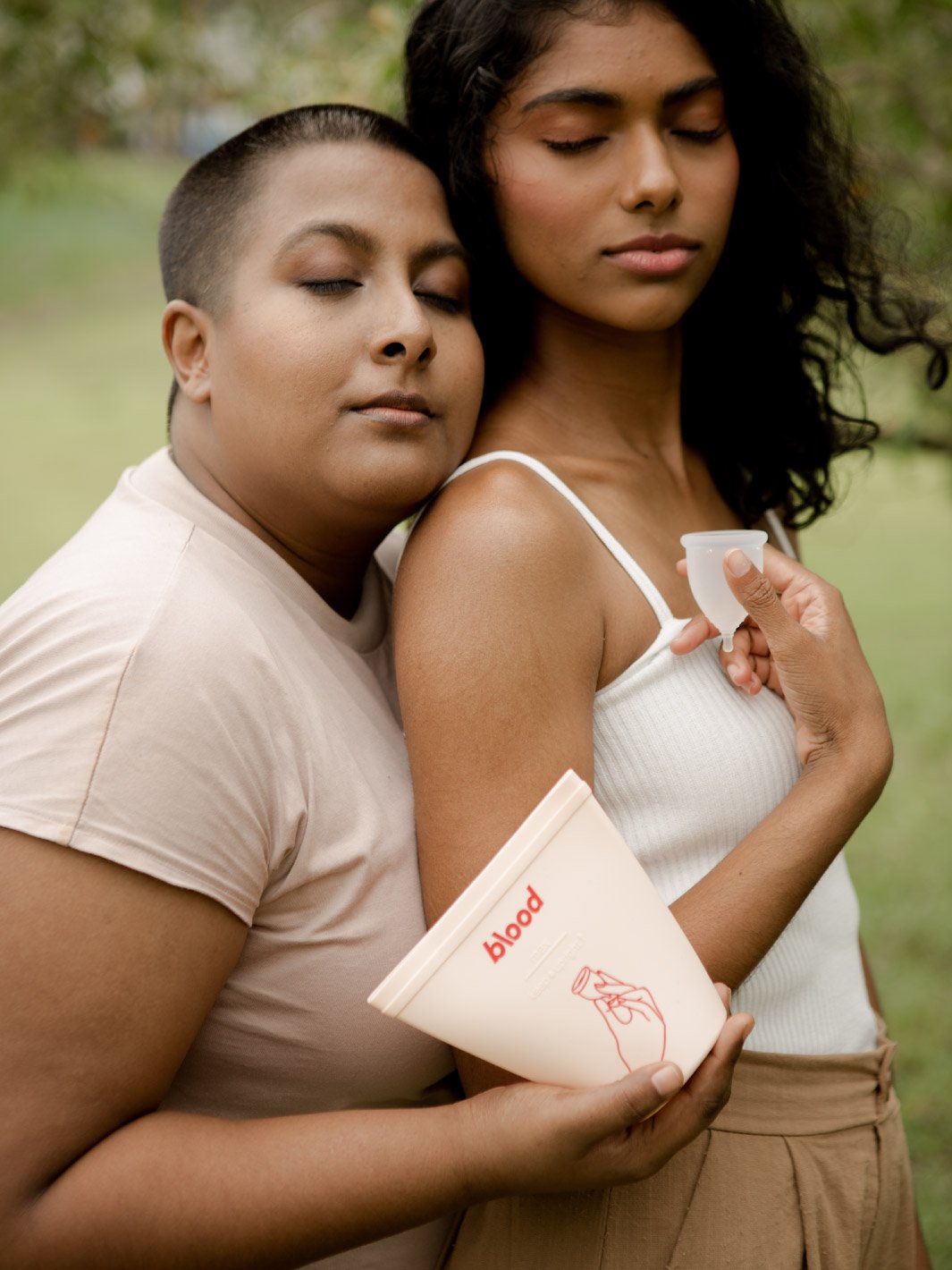 2 girls in a field holding a menstrual cup and sanitising pouch